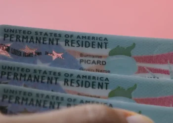 Carte verte américaine (Green Card) devant un drapeau des États-Unis, illustration du projet de caution de 100 000 dollars.